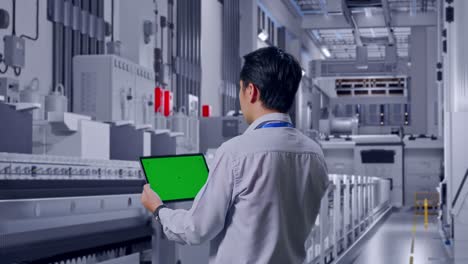 back view of an asian male professional worker standing at pharmaceutical factory, vaccine production facility, checking on tablet with green screen and look at the factory once
