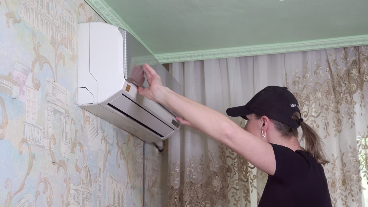 Woman opens air conditioner and inspects condition of air filters.