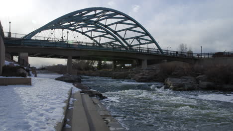 speer boulevard bridge over south platte river in denver, colorado with snowy riverbank in winter