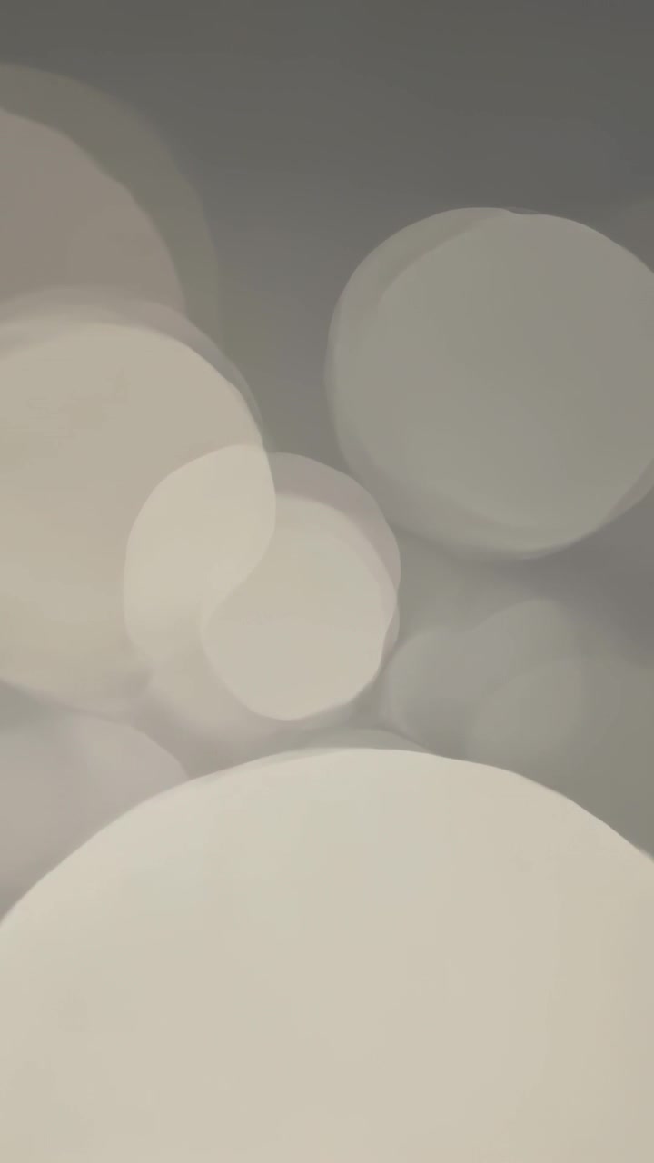 Vertical video: Moving bokeh field responding to focus change on neutral grey backdrop, brightening