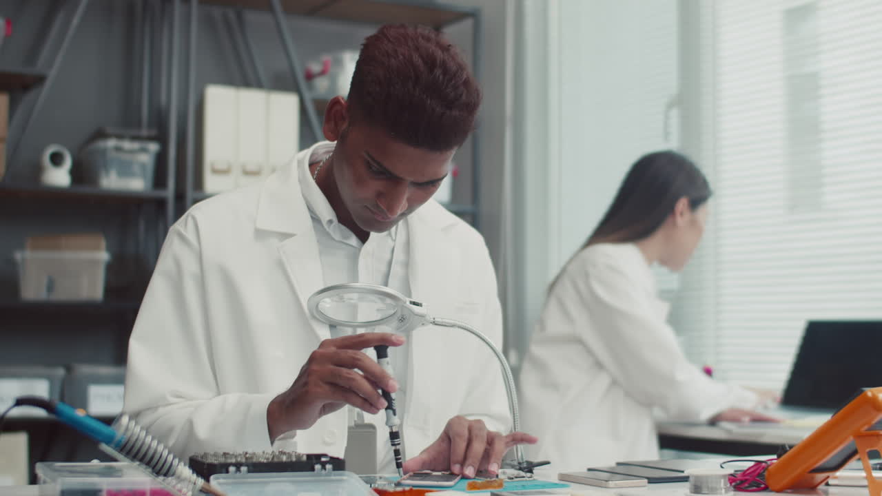 Engineer Unscrewing Broken Component of Smartphone at Table