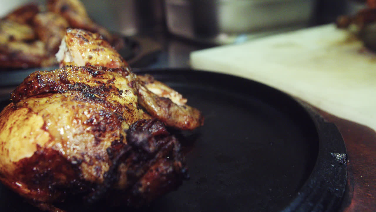 eautiful slow motion shot of a chef placing a piece of charcoal roasted chicken on a wooden plate with other pieces of chicken inside a restaurant kitchen.