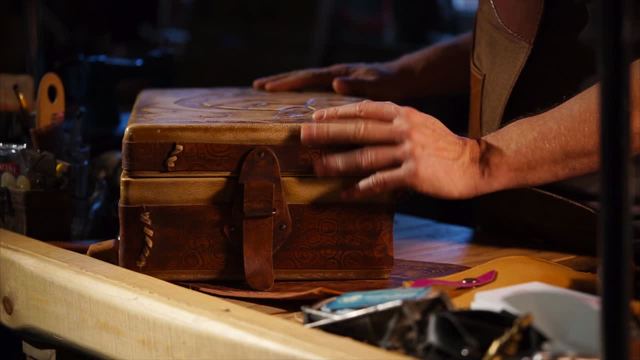 Close-up of hands handling a decorative leather box on a workbench