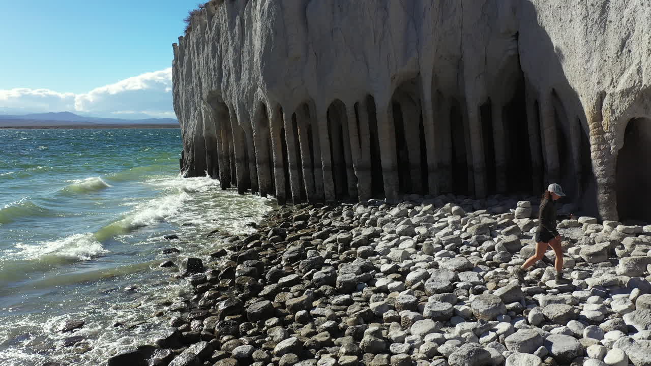 вид с воздуха на одинокую женщину, идущую по скалистому берегу озера кроули у колонн, чудо природы и живописная достопримечательность калифорнии, сша