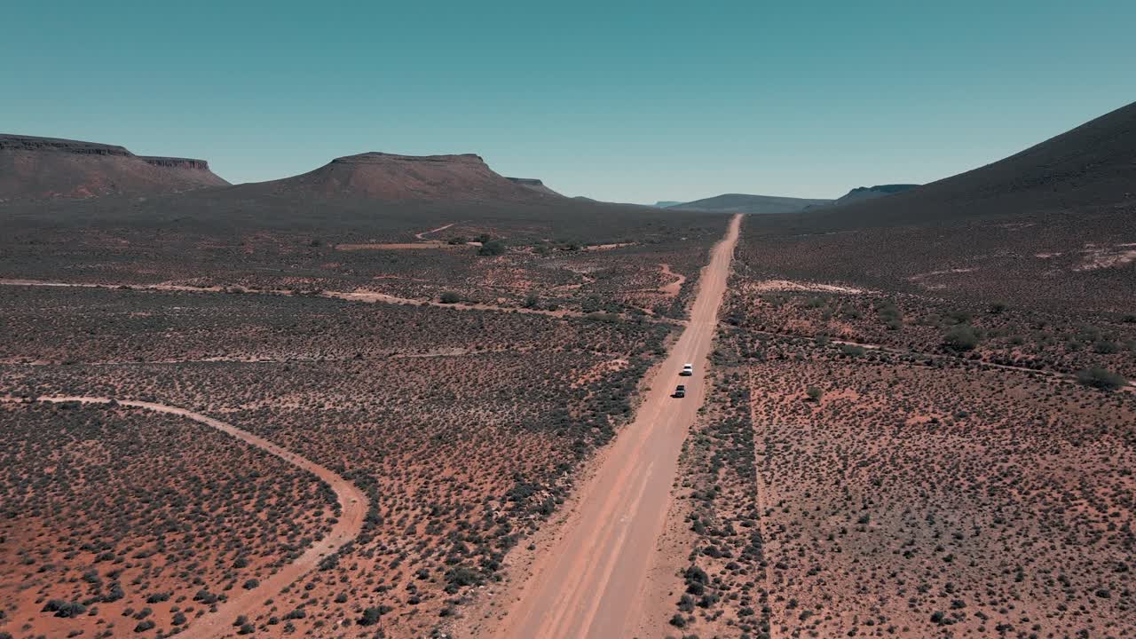 Two vehicles drive in convoy over a vast, empty landscape of the Karoo in South Africa
