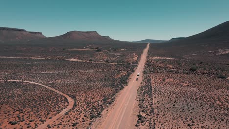 two vehicles drive in convoy over a vast, empty landscape of the karoo in south africa