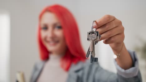 shot of apartment keys extended on hand toward camera, pink-haired woman dressed in suit holds documents and hands over keys, real estate agent, flat owner, receiving room for use