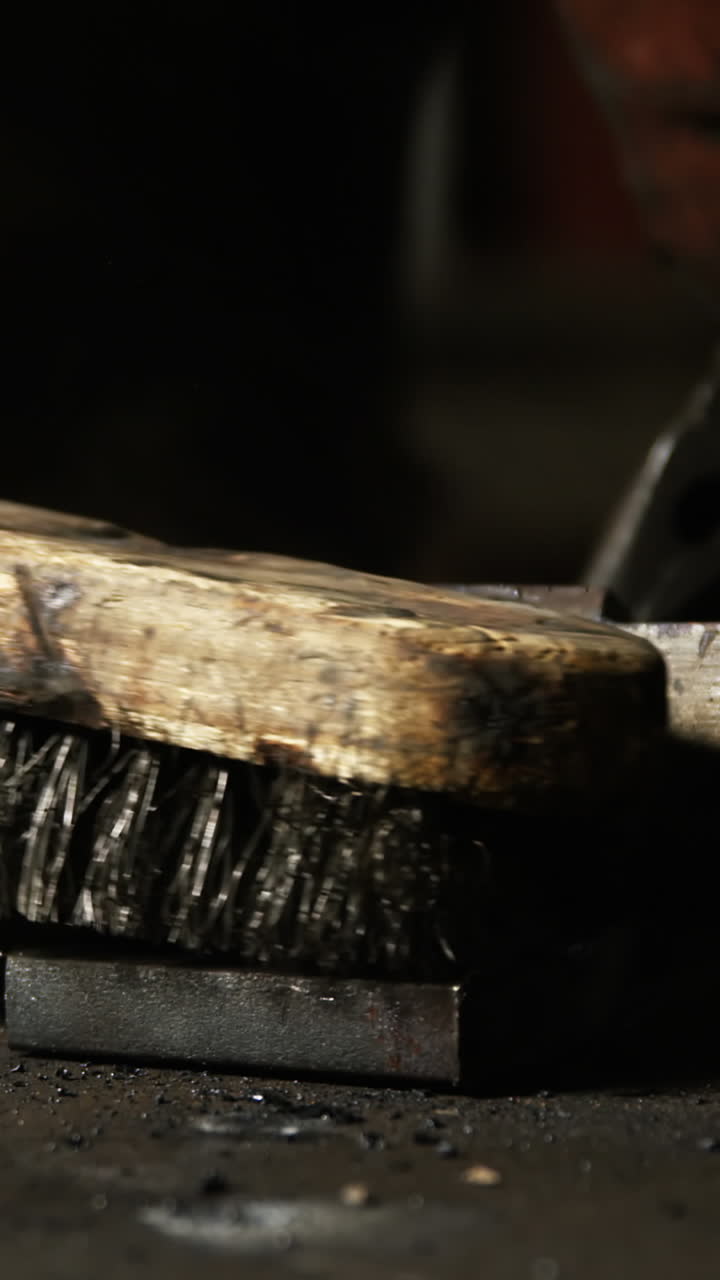 Hands of welder using wire brush on a piece of metal