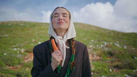 mujer sonriente comiendo zanahoria en el campo verde de la granja. chica divertida de primer plano mordiendo bocadillo