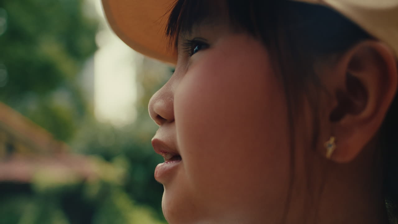 Young girl in a yellow cap outdoors, looking upward with a joyful expression