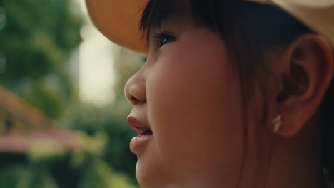 young girl in a yellow cap outdoors, looking upward with a joyful expression