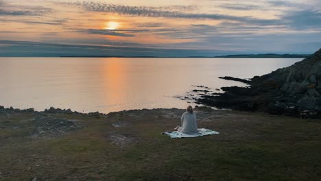 Aerial-of-Beautiful-Young-Hiker-sitting-on-top-of-mountain-meditating-on-blanket