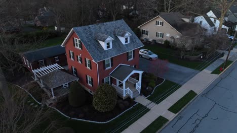 aerial approaching shot of red single family house in american residential area during golden hour