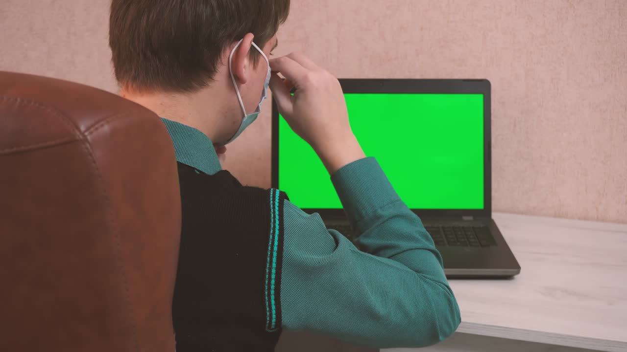 un hombre se pone una máscara de protección facial a sí mismo y al interlocutor por llamada de video y comienza a escribir en una computadora portátil, seguridad epidemiológica, trabajo remoto, pantalla verde