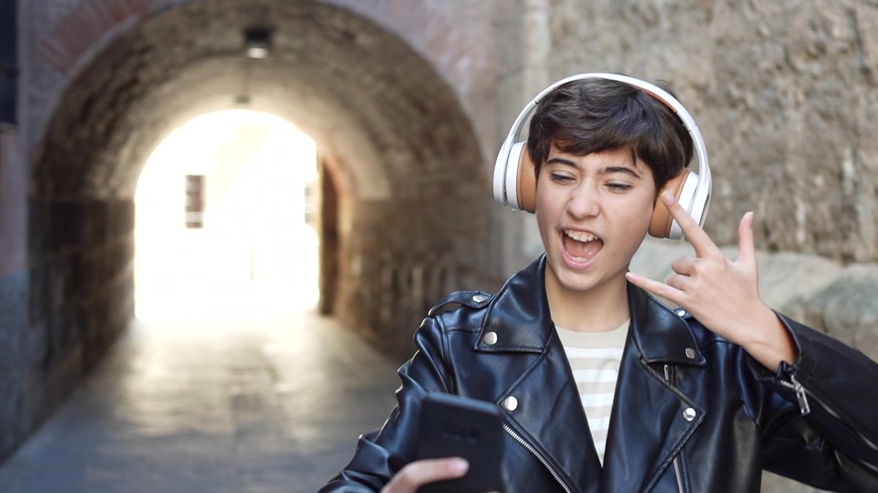 Una persona giovane che ascolta musica con entusiasmo all'aperto, vestita con un'elegante giacca di pelle.