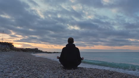 Time-lapse-video-of-man-meditating-on-stoney-seaside-as-sun-rises-over-horizon-by-sea
