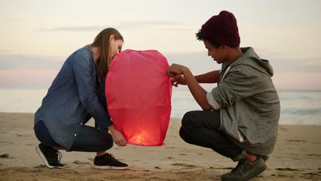 cute multi ethnic couple holding red paper lantern before launching. attractive woman with her african boyfriend holding lantern