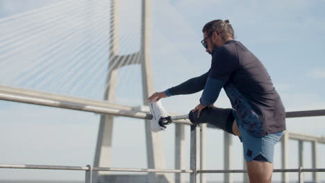 back view of a sportsman with disability putting leg on post and stretching muscles