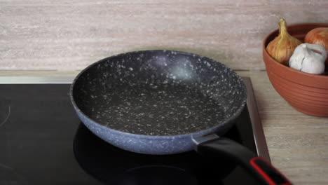 caucasian right hand pours oil in black frying skillet on stove, close