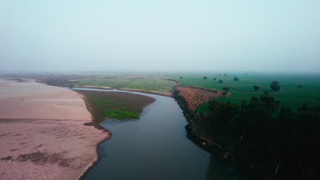 River-winding-through-a-green-landscape-at-dawn,-misty-air,-aerial-view