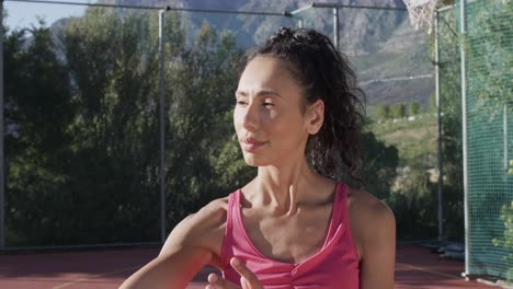 Portrait-of-biracial-female-basketball-player-spinning-ball-on-sunny-court,-in-slow-motion