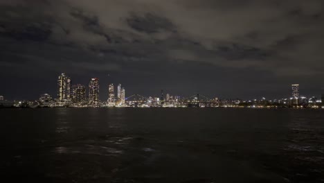 Ein-Ruhiger-Nächtlicher-Blick-Auf-Die-Brooklyn-Bridge-Und-Die-Skyline-Von-Manhattan,-Mit-Den-Lichtern-Der-Stadt,-Die-Sich-Unter-Einem-Dramatischen-Wolkenhimmel-Im-East-River-Spiegeln-Und-Die-Urbane-Schönheit-Von-New-York-City-Einfangen