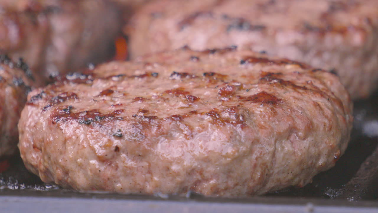 Side View of Juicy Beef Burgers Cooking on BBQ with Flames Coming from Gas Fired Stove Below. High Quality ProRes Food Footage.