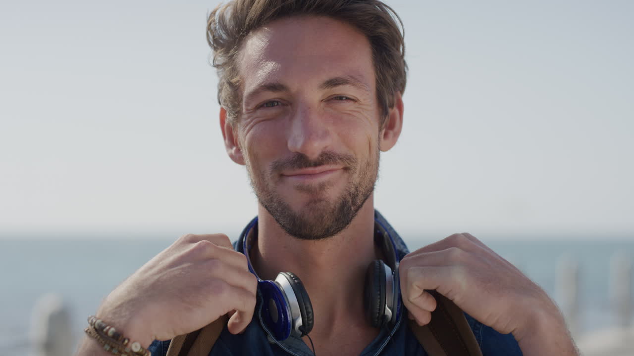 portrait happy young man tourist smiling enjoying warm summer day on seaside wind blowing hair slow motion