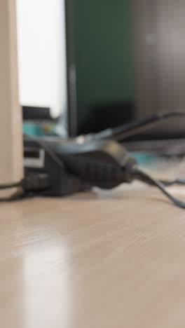 una vista de cerca de una mano que lleva gafas negras en un escritorio de madera en un entorno de laboratorio, con herramientas electrónicas en la mesa y cables alrededor