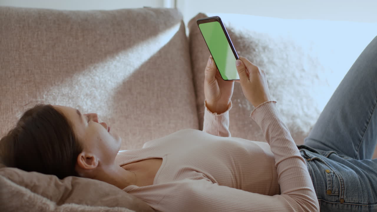 mujer relajándose en el sofá usando el teléfono con pantalla verde