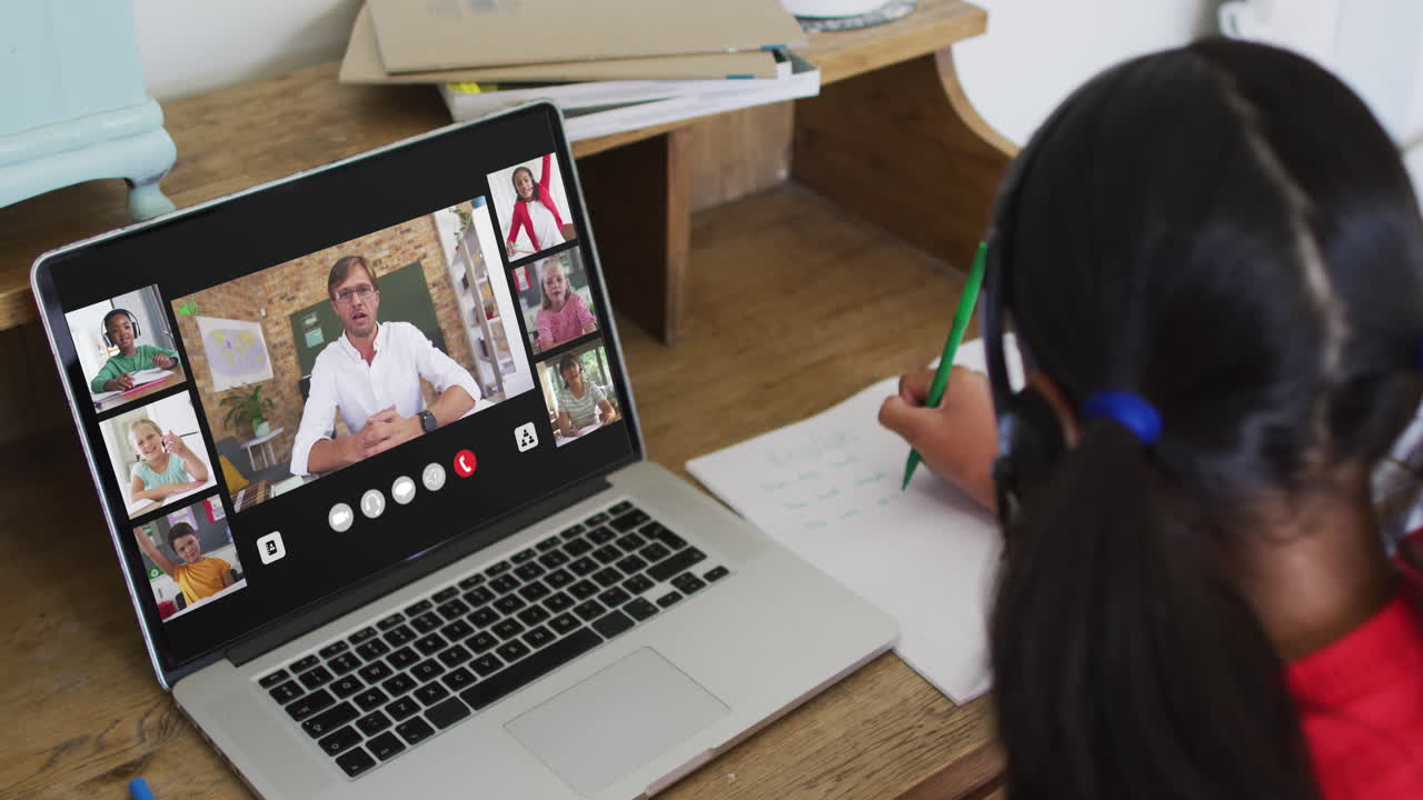 Schoolgirl using laptop for online lesson at home, with diverse teacher and class on screen
