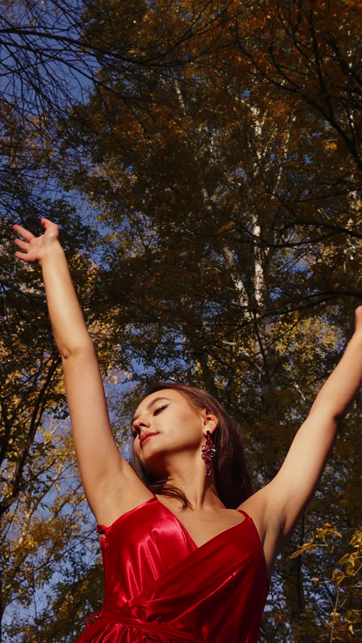 A Graceful Woman in Red Dress Embracing Nature's Beauty Beneath a Radiant Autumn Sky Surrounded by Golden Leaves and Majestic Trees