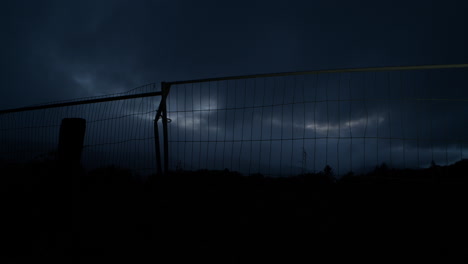 silhouette of metal fence, rural scene during nightfall with dark clouds in evening sky