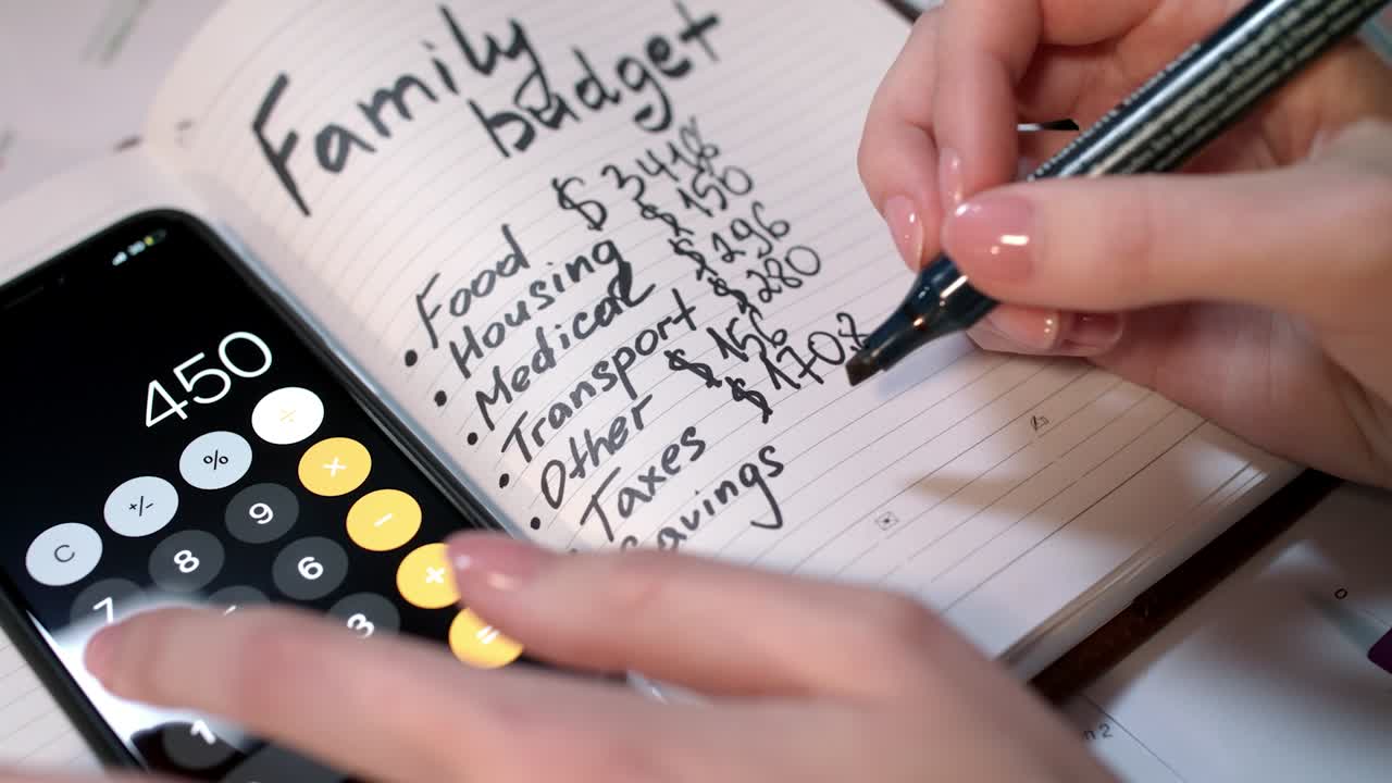 Kvinde beregner familiebudget på lommeregner og skriver i notesbog