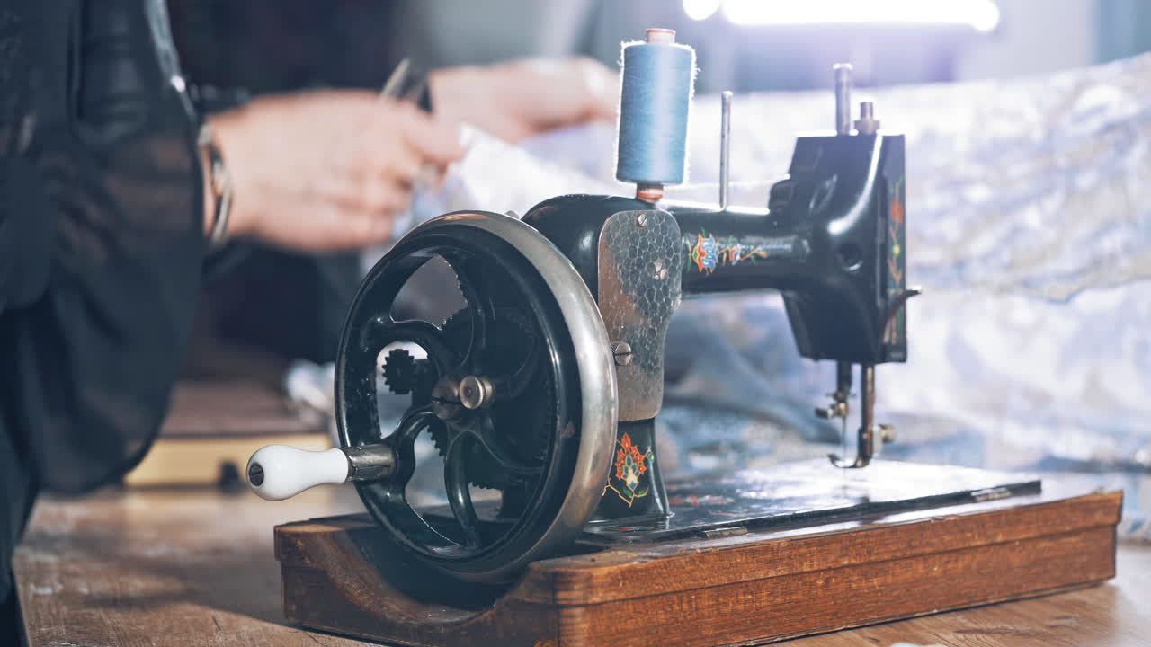Old black sewing machine on the background of a female tailor at work in atelier. Professional seamstress working in the workshop with beautiful material.