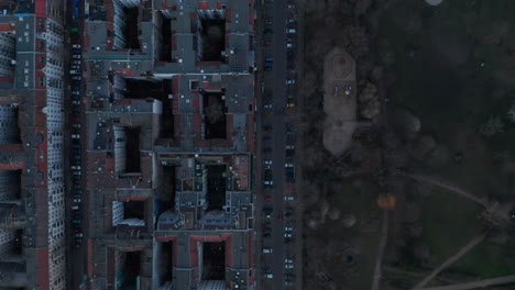 Top-down-view-of-rooftop-of-residential-houses-with-vehicles-parked-and-moving-across-lane-surrounded-with-trees-during-morning-in-Berlin,-Germany