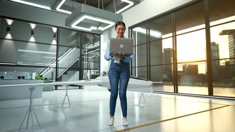 cuerpo lleno de una trabajadora profesional asiática de pie con su computadora portátil con proyecto de drones, instalación industrial de alta tecnología, trabajando continuamente