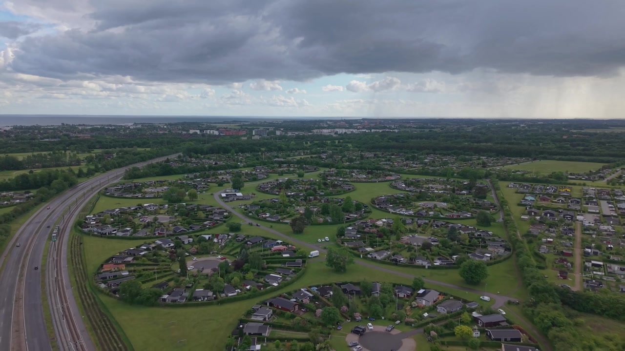 Riprese con drone che si allontanano per rivelare Haveforeningen Harekaer, con affascinanti cottage da giardino incorniciati da nuvole di pioggia scure e un'atmosfera scandinava drammatica