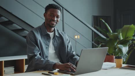 portrait of smiling african american businessman with laptop at office desk