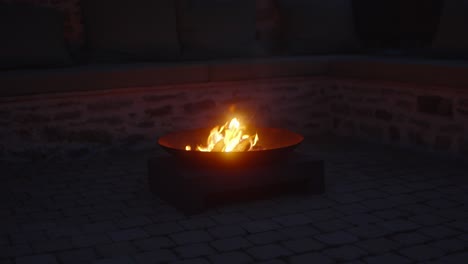 closeup of flames in a fire bowl flickering on a gentle wind outdoors at night illuminates atmospheric backyard, creating a cozy and tranquil scene