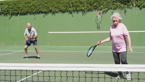 feliz pareja de adultos caucásicos jugando como equipo de dobles en una cancha de tenis al aire libre después de jugar un juego