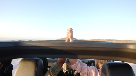 Hands-of-a-couple-are-intertwined-above-a-car's-dashboard-on-a-road-trip