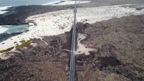 Luftaufnahme-Einer-Langen,-Einsamen-Straße,-Bedeckt-Mit-Sand,-Neben-Dem-Meer-Und-Einem-Felsigen-Strand