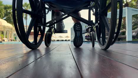 persona en silla de ruedas sentada en una terraza o patio con vistas a la piscina - vista en ángulo bajo de la silla de ruedas y los pies