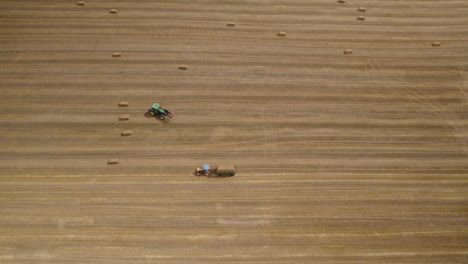 Hay-Harvest-Agriculture-Machinery,-Tractors-in-Agricultural-Farmland-Field-Working-Moving-and-Driving-Carry-Load-Hay-Bales,-Farm-Work-Aerial-View