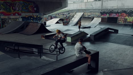 young teens practicing together on bmx bike and skate board at skate park.