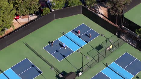 aerial view circling, looking down over young adult foursome playing pickleball on blue sunny tennis court