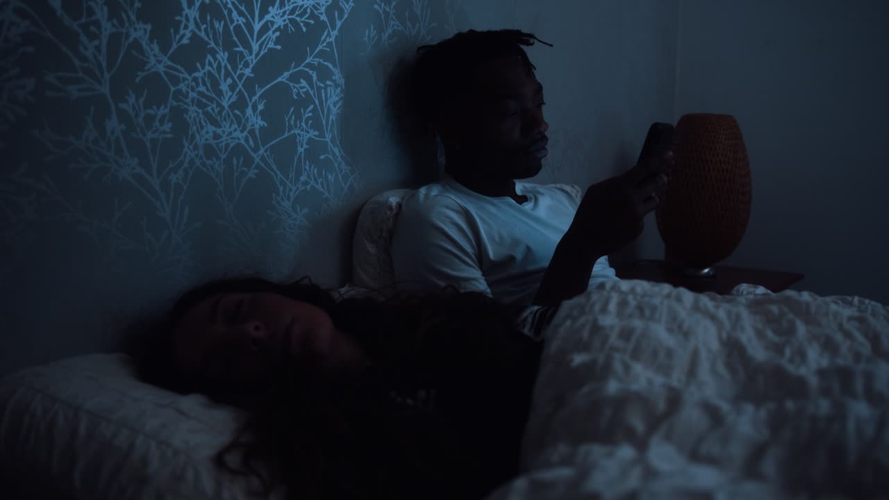 мужчина смотрит на партнера, глядя на смартфон, не спит до поздней ночи.