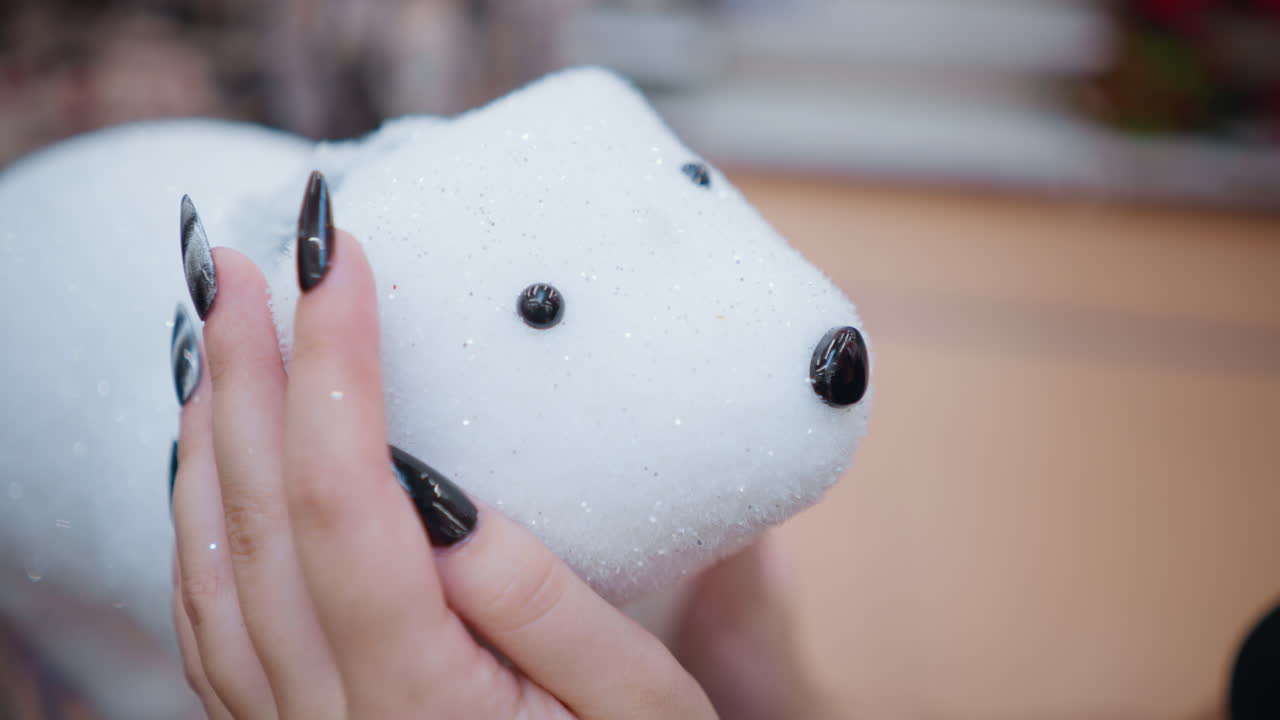 검은색 은 손을 가진 여성 손의 클로즈업, 플러시 하 북극 을 들고, 휴일 장식으로 가득 찬 부드럽게 흐릿한 배경에 복잡한 세부 사항을 보여줍니다.