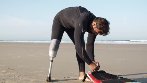 vertical motion of a male surfer with prosthetic leg tying leash on surfboard